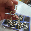 A hand holds a small metal wire puzzle chain with various interlocking rings and shapes.