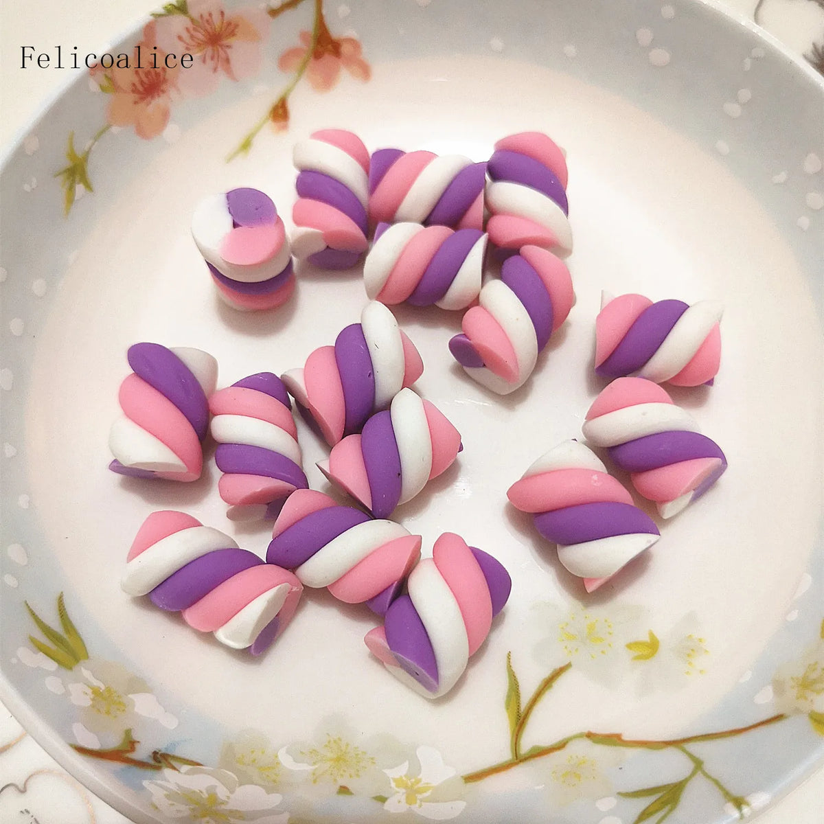 A collection of pink and purple striped polymer clay marshmallow charms arranged on a white plate.