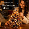 A woman is decorating a glowing Halloween tree kit with colorful lights and ornaments.