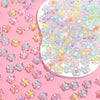 A collection of colorful transparent acrylic flower beads scattered on a pink background.