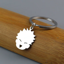 A white silhouette of a spiky-haired anime character charm attached to a silver keychain ring, resting on a wooden surface.