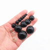 A hand holds several black plastic safety eyes for amigurumi with locking washers.