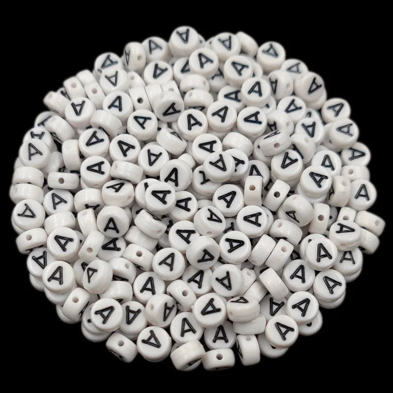 A close-up view of numerous white acrylic alphabet letter beads scattered on a dark background.