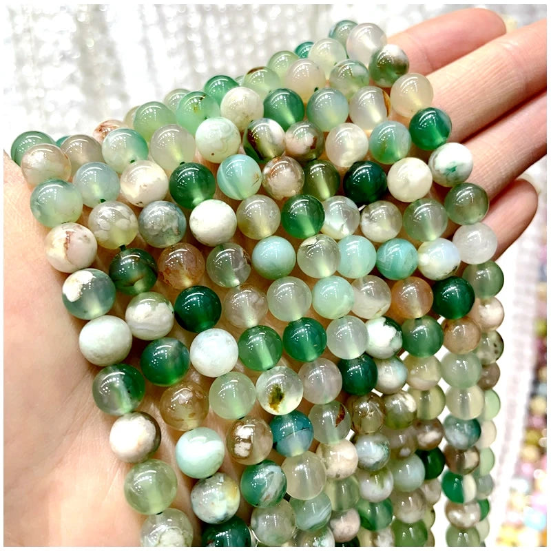 A hand holds a strand of natural stone beads featuring various shades of green, white, and amber stones.
