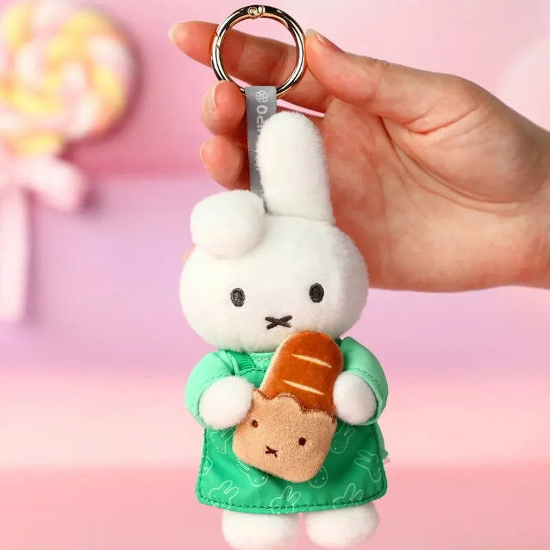 A white bunny plush keychain charm holding a small brown pastry in a green fabric pouch.