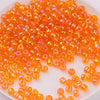 A pile of small, translucent orange glass rice beads for DIY jewelry and crafting.