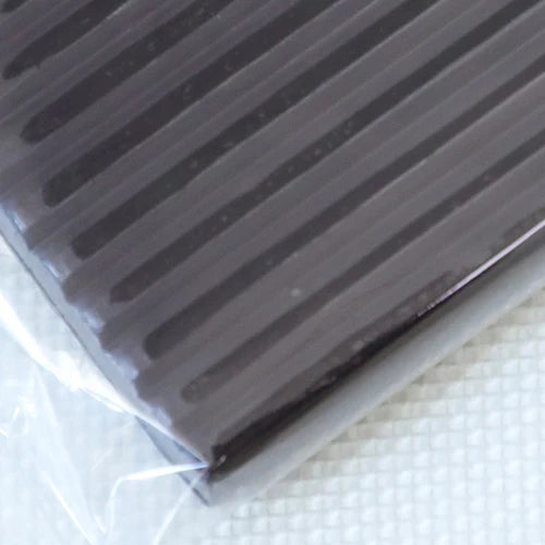 A close-up view of a dark gray polymer clay kit with ribbed texture, packaged in clear plastic.