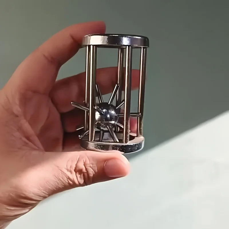 A hand holds a multi-layer stainless steel puzzle cage brain teaser with a central spinning mechanism.
