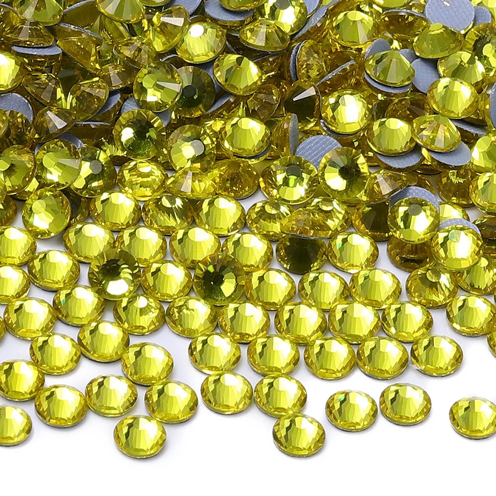 A close-up view of numerous round, faceted yellow glass crystal rhinestones scattered on a white surface.
