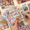 A hand holds a stack of Kawaii embroidery-style sticker sheets featuring cute animal and food designs.