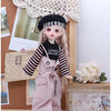 A doll wearing a pink outfit and a black Superbike hat is displayed next to a wooden box.