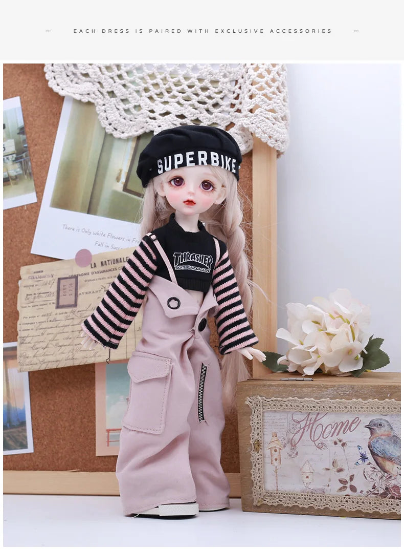A doll wearing a pink outfit and a black Superbike hat is displayed next to a wooden box.