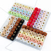 A collection of 35 plush fur pom pom beads in various colors and shades arranged in small plastic trays for jewelry making