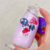 A hand holds a purple liquid bottle containing pink and blue squishy fruit toys for fidgeting.