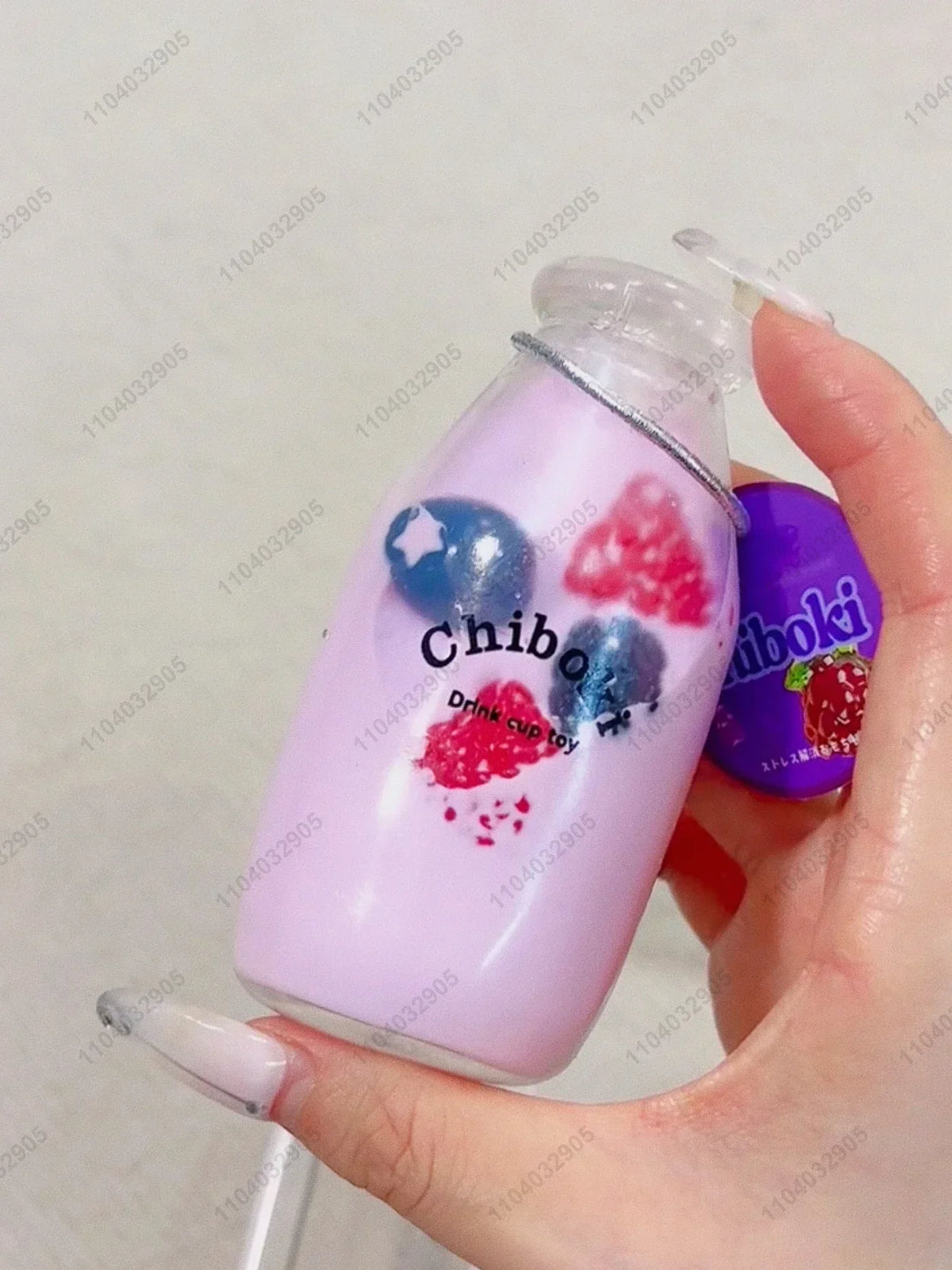 A hand holds a purple liquid bottle containing pink and blue squishy fruit toys for fidgeting.