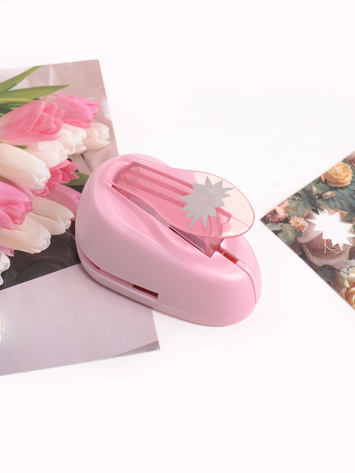 A pink lever action embosser tool is shown next to a bouquet of pink and white flowers.