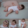 A newborn Reborn baby doll named Maddie with soft body and detailed 3D skin lying on a white surface.