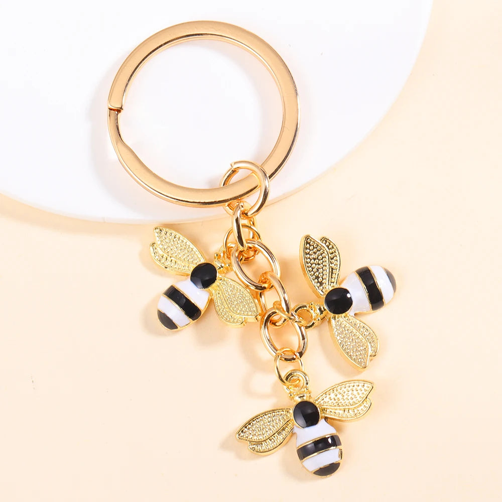 Gold-toned enamel flower keychain featuring a bee design with black and white stripes