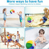 A young boy is playing with a rainbow striped inflatable beach ball in a bathtub.