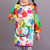A child wearing a colorful, paint-splattered long-sleeve smock and dining bib with a pocket.