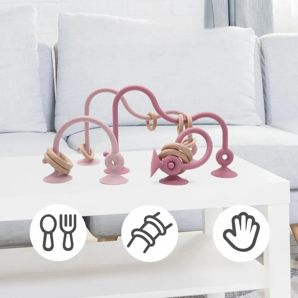 A set of pink silicone teether rings for babies displayed on a white table.
