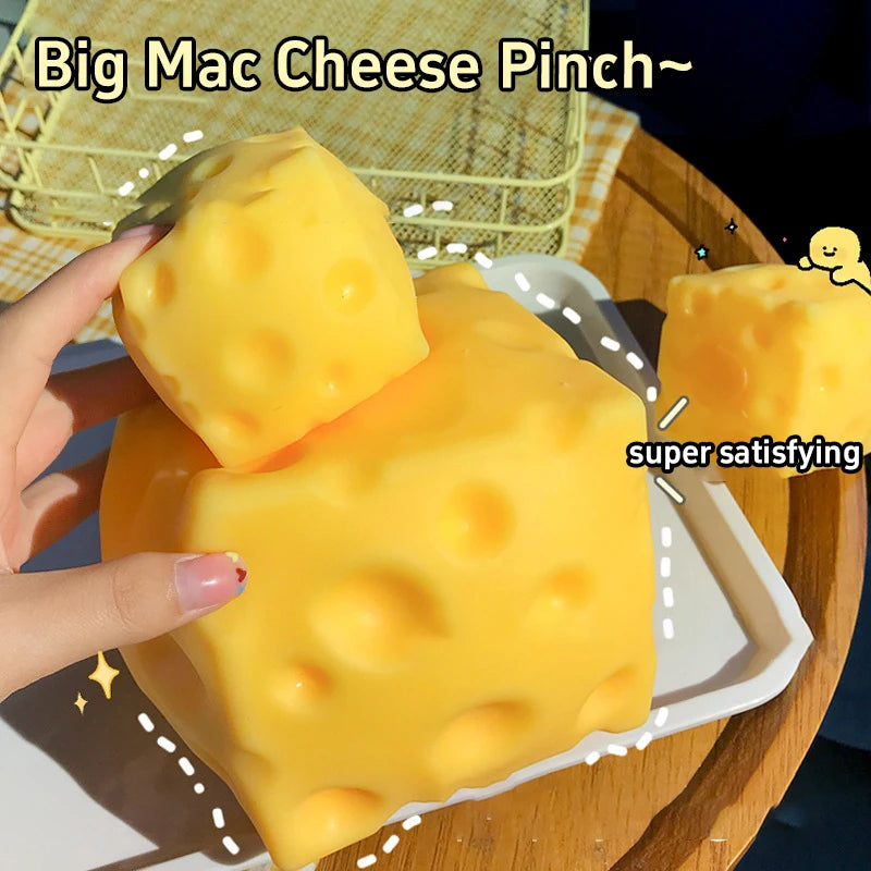 A hand holds a large yellow cheese-shaped squishy fidget toy on a white plate.