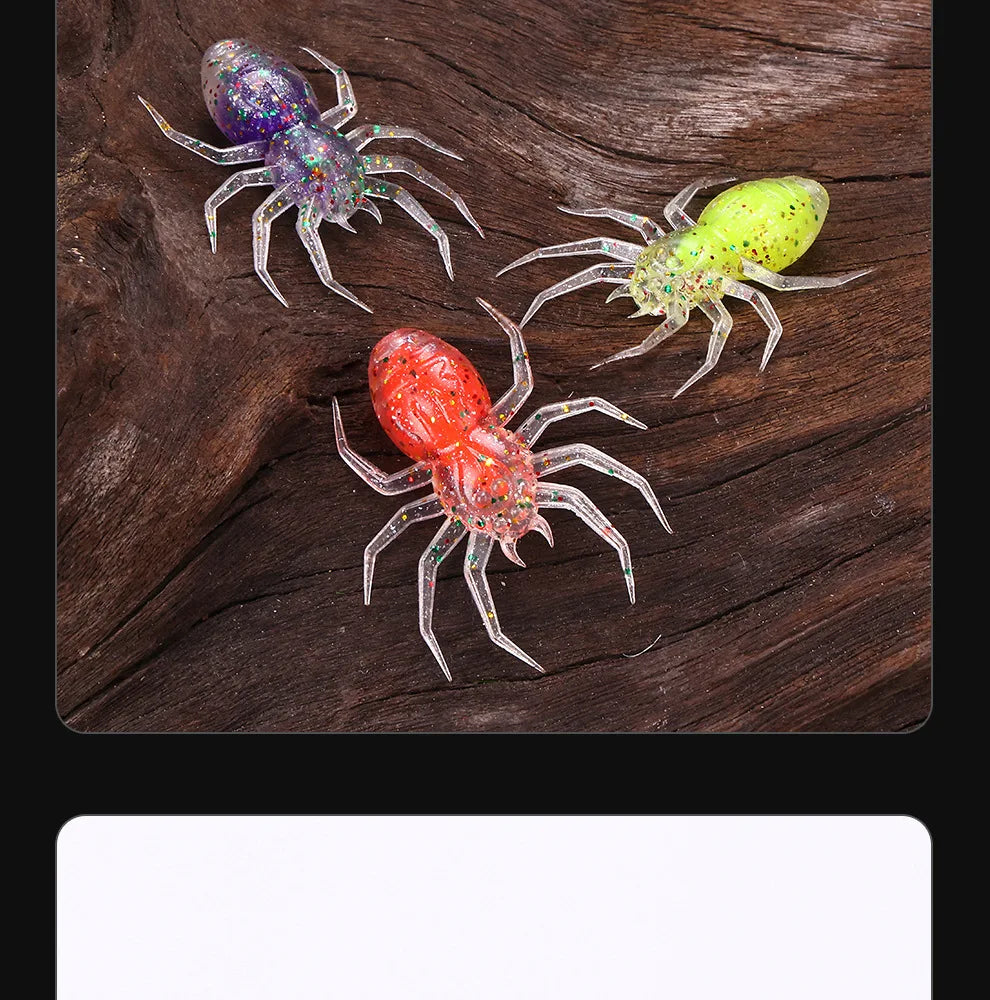 A close-up of three realistic, laser-reflective spider soft bait lures in various colors resting on dark wood.