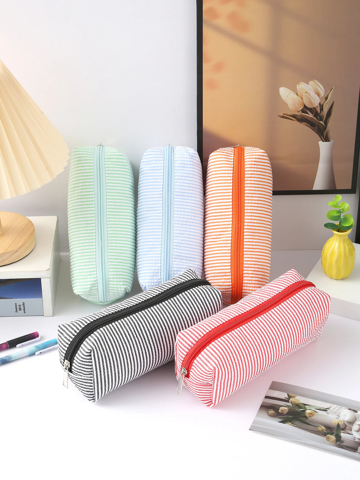 A collection of striped canvas pencil cases in mint green, light blue, and orange are displayed on a white surface.
