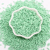 A pile of light green polymer clay slice sprinkles in a white bowl on a white background.