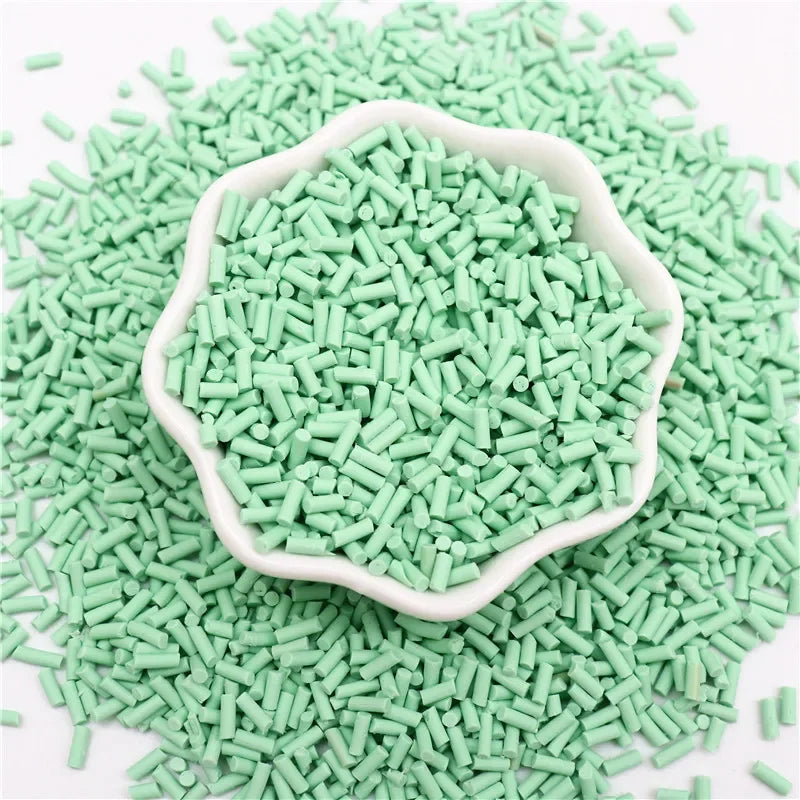A pile of light green polymer clay slice sprinkles in a white bowl on a white background.