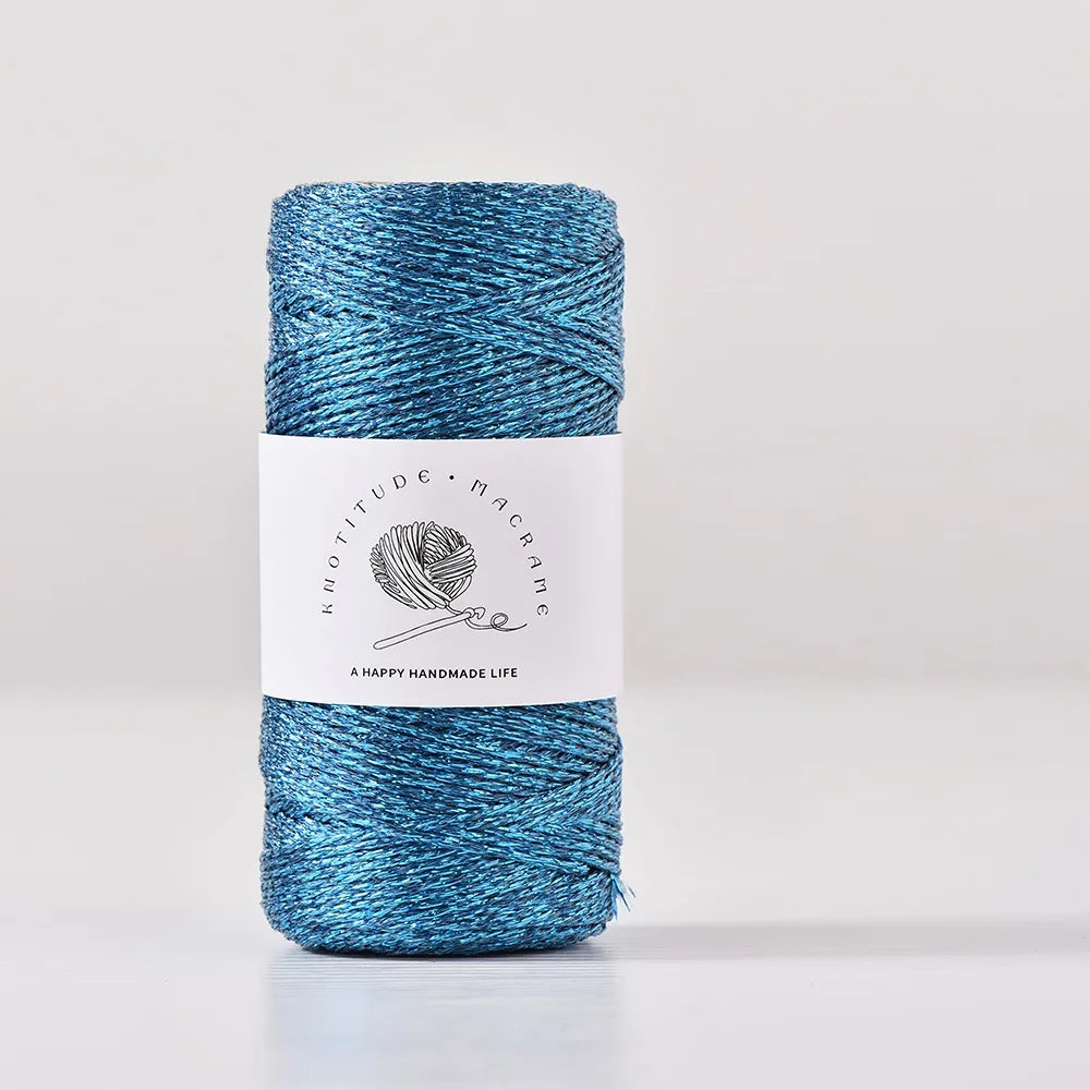 A spool of metallic blue glitter yarn for knitting and crochet with a white label.