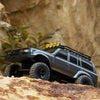 A black 1:18 scale remote control off-road climbing car with a roof rack and yellow lights is positioned on a rocky surface.