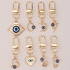 A set of gold-colored cartoon evil eye keychains featuring various designs like an eye, crescent moon, and lightning bolt.