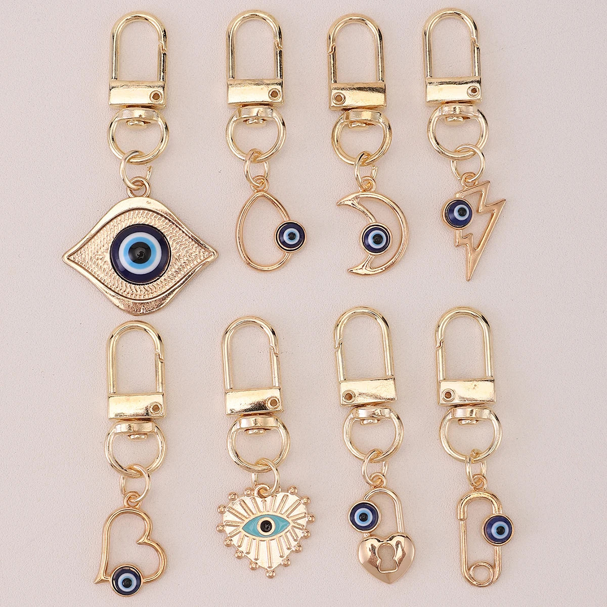 A set of gold-colored cartoon evil eye keychains featuring various designs like an eye, crescent moon, and lightning bolt.