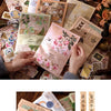 A hand is holding a vintage sticker and paper combo kit for crafting, featuring various aged papers and stickers.