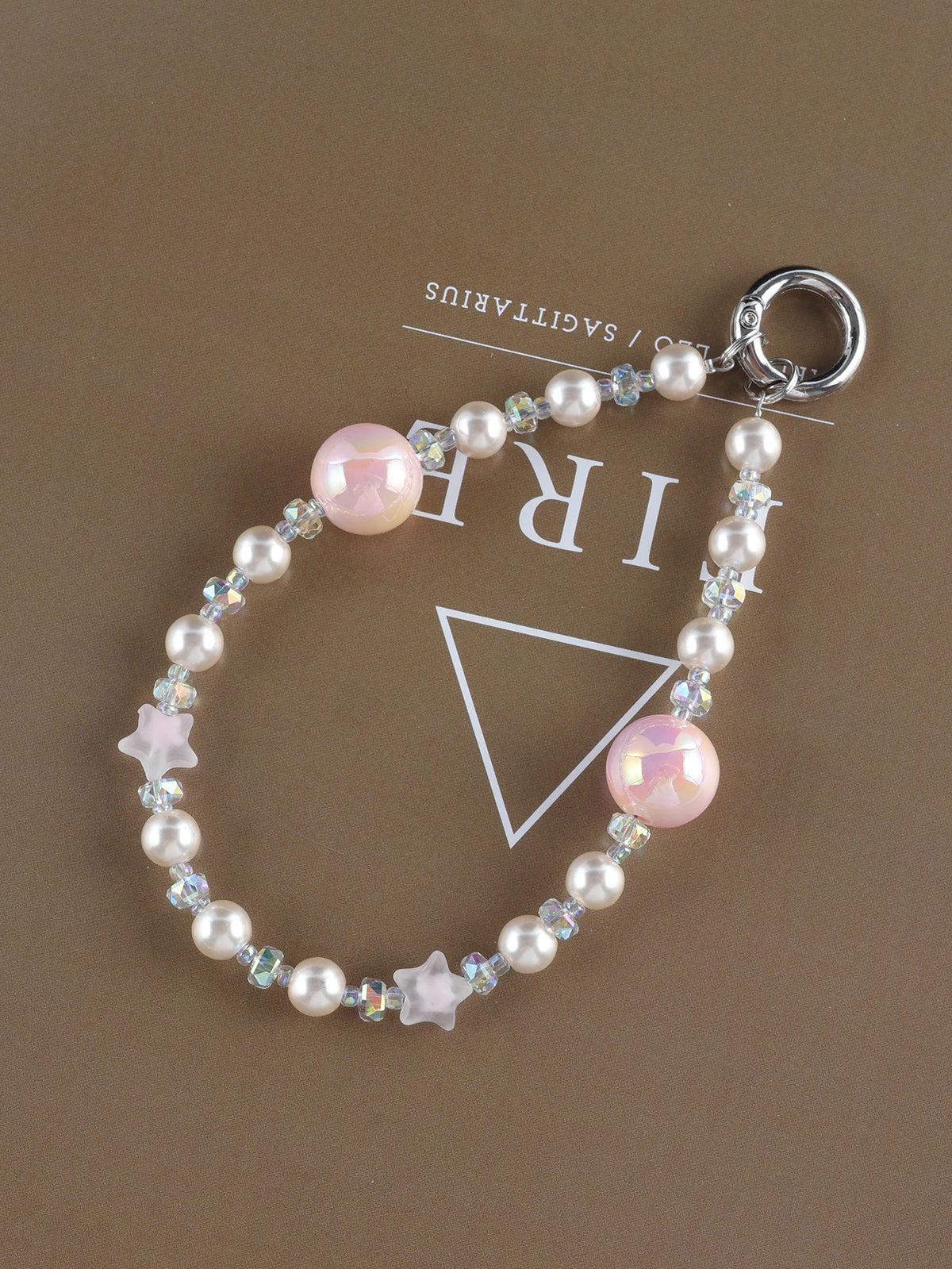 A necklace featuring pink and clear pearls and a star charm, displayed against a brown background.