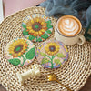 A set of floral diamond painting coasters featuring yellow and green flowers on a woven mat with a latte cup and a gold spoon