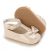 A pair of light beige lace-trimmed baby girl moccasin shoes with a bow shown from the sole view.