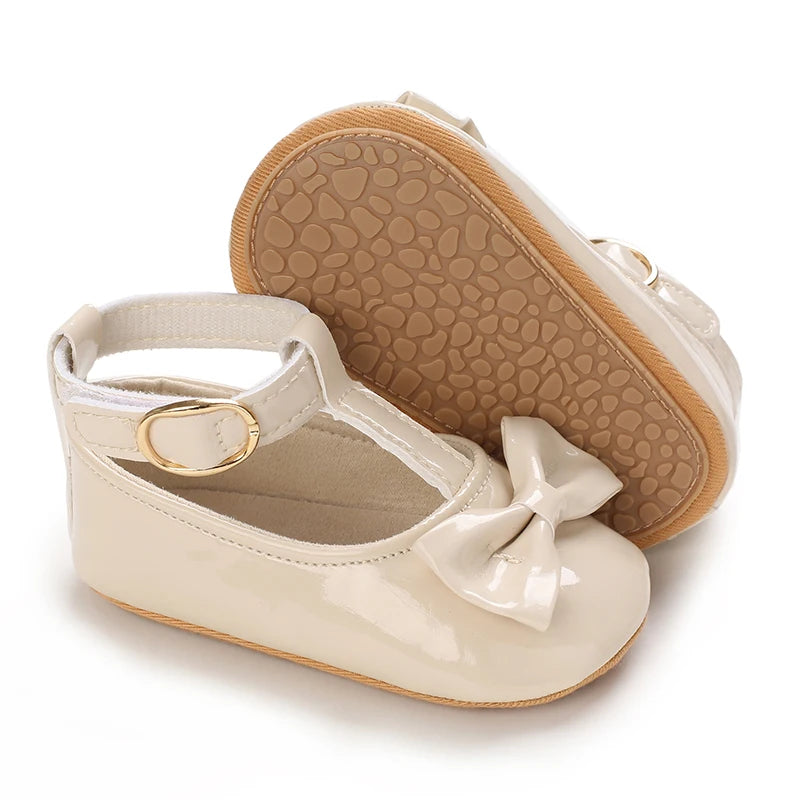 A pair of light beige lace-trimmed baby girl moccasin shoes with a bow shown from the sole view.