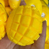 A close-up of a bright yellow mango squishy stress relief ball with a textured surface being held in a hand.