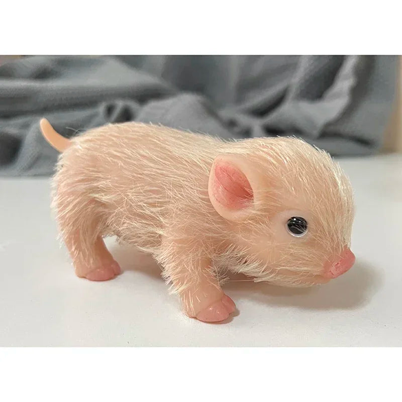 A small, soft pink silicone reborn piglet doll with realistic features is shown against a light background.