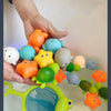 A hand is placing various glow-in-the-dark plastic animal toys into a white basin of water.