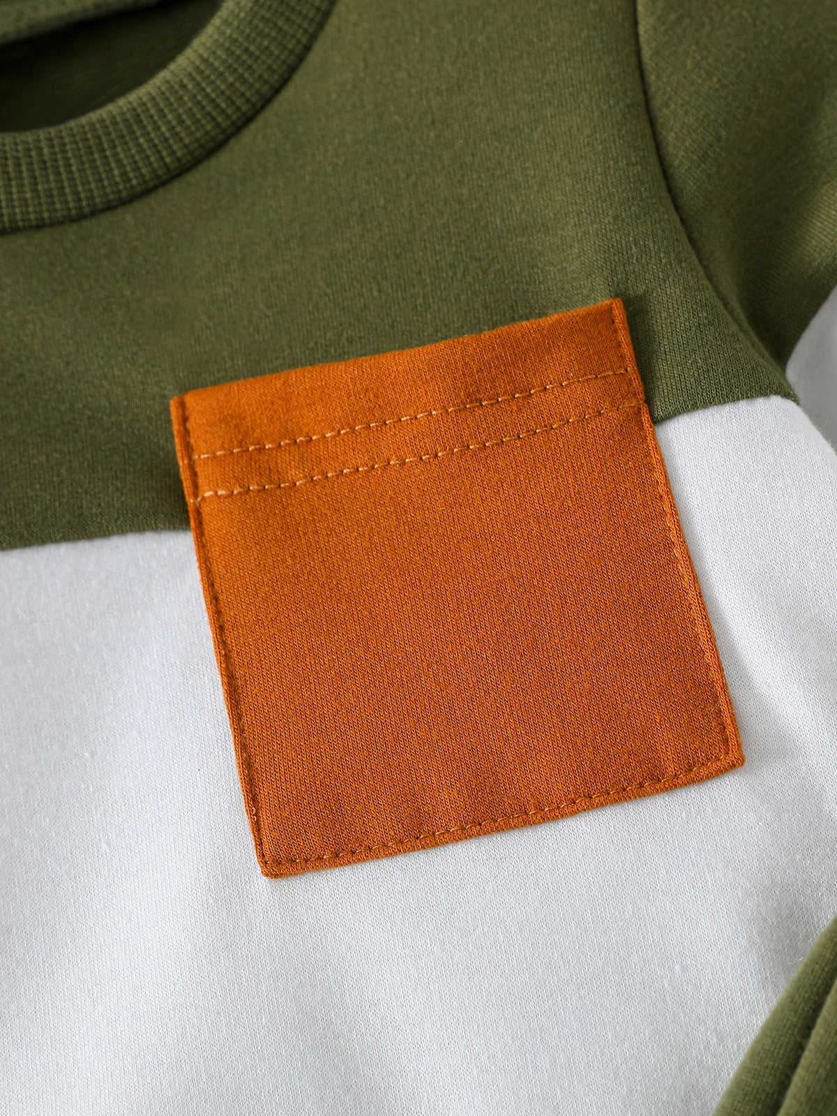 A close-up of an orange fabric patch sewn onto a olive green and white sweatshirt set.