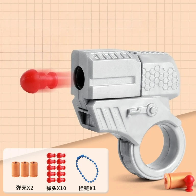 A silver mini shell-ejecting fidget pistol with a ring, showing various components like a red pellet and small shells.