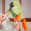 A hand is holding a green and orange parrot plush finger puppet.