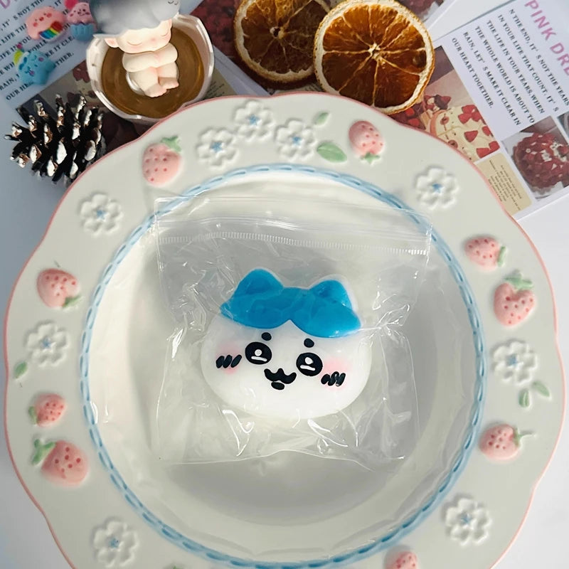 A white squishy toy shaped like a smiling face with blue accents is sealed in a clear plastic bag on a decorative plate.