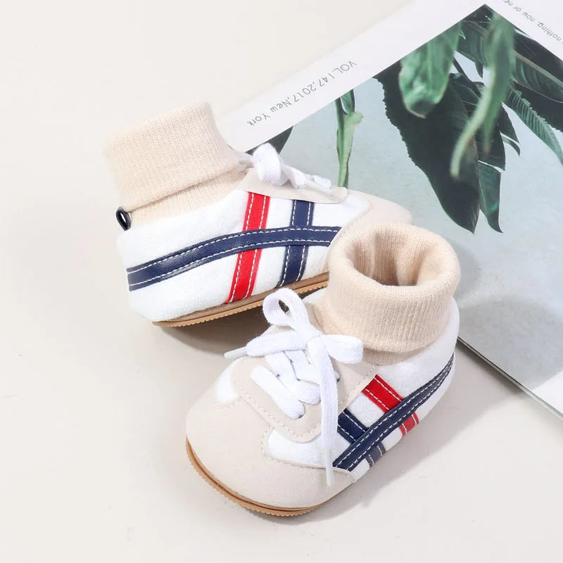 A pair of beige ankle-hugging baby booties with white fabric and navy and red stripes on the side