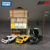 A diorama featuring a miniature Japanese-style building and four die-cast sports car models.
