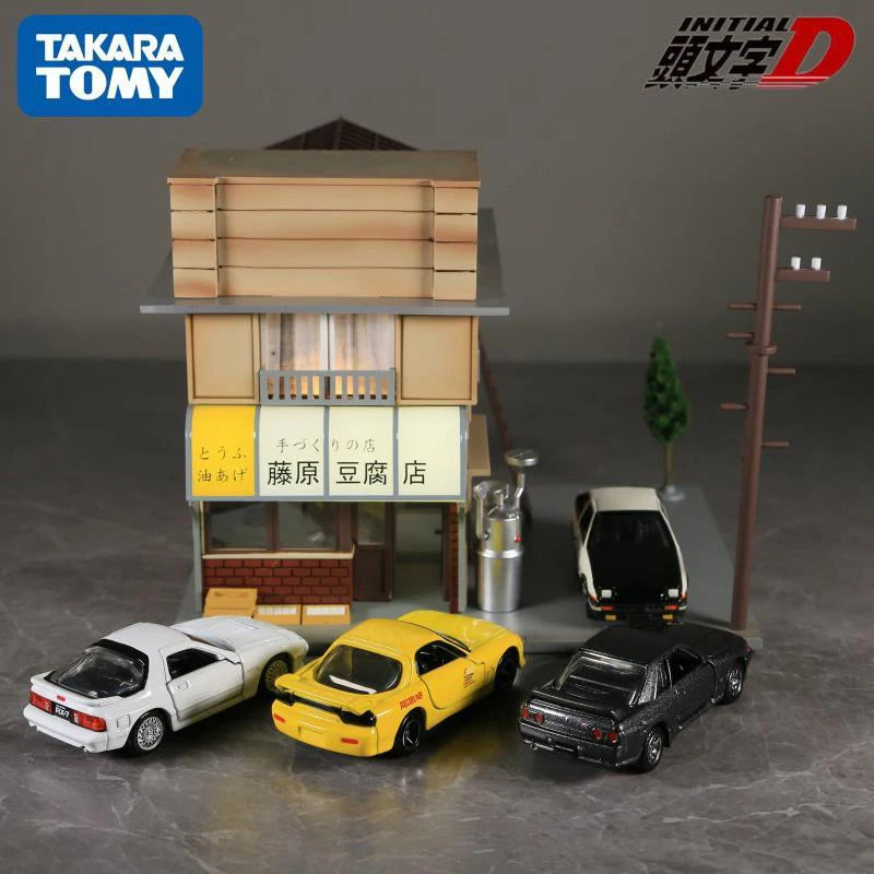 A diorama featuring a miniature Japanese-style building and four die-cast sports car models.
