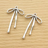A pair of silver alloy bow charms for jewelry making displayed on a light brown surface.